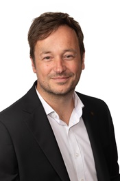 A portrait of James Grayson wearing a white business shirt and black suit jacked smiling against a white void.